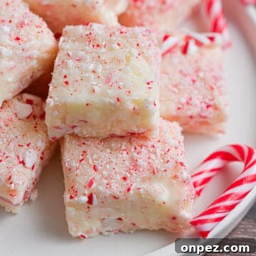 A pile of white chocolate peppermint fudge is on a white plate surrounded by small candy canes.