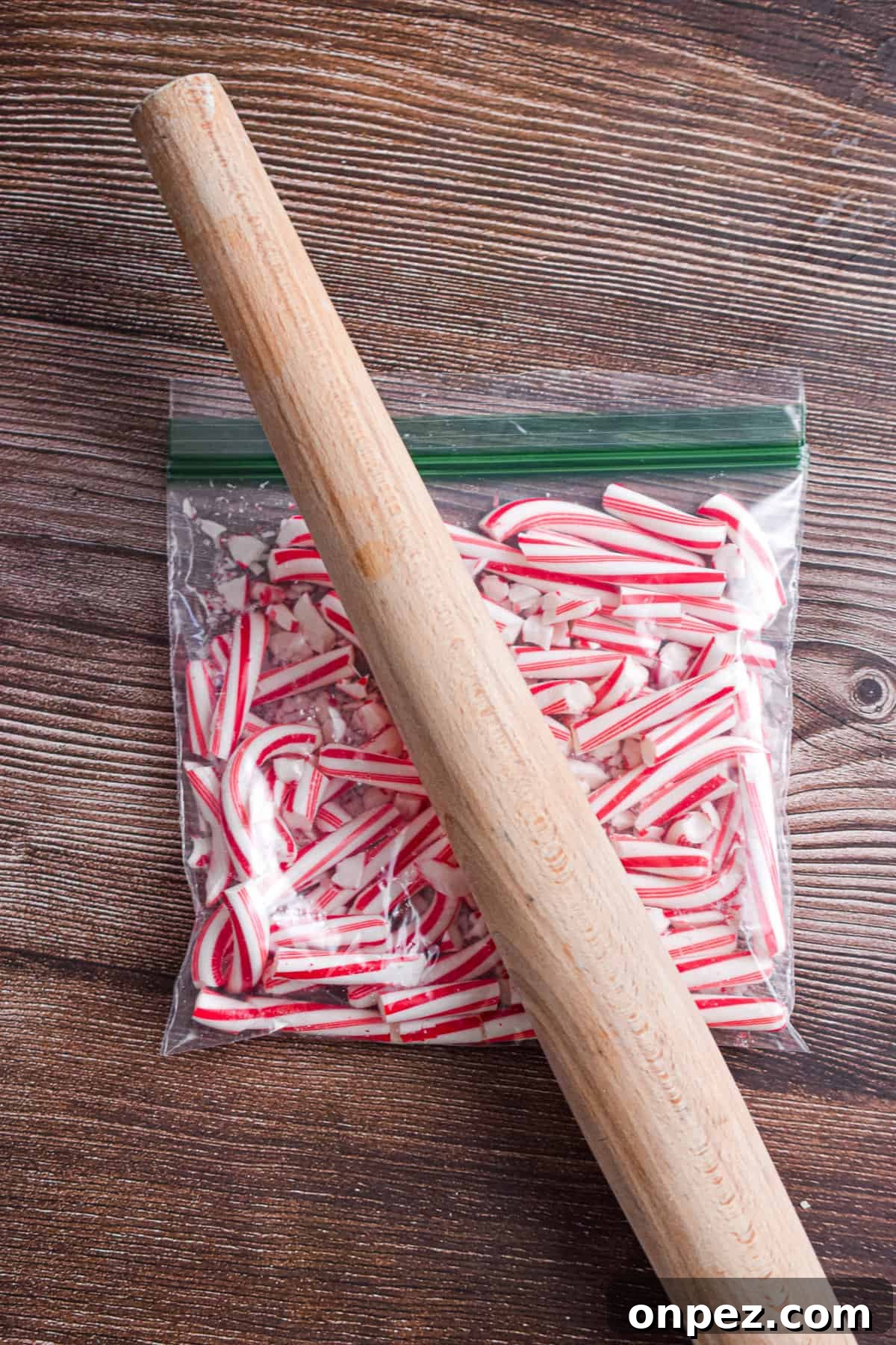 A rolling pin is crushing the candy canes in a Ziploc bag.