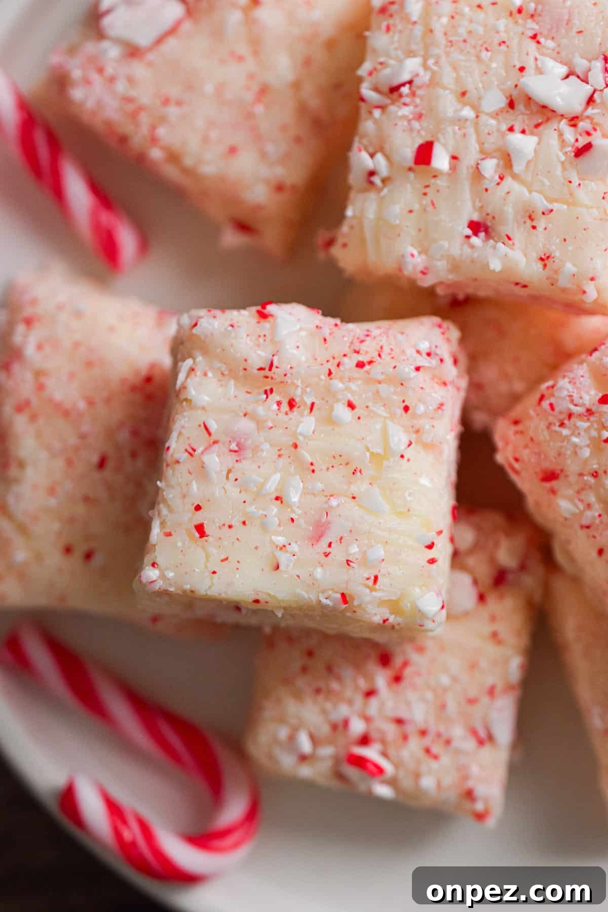 White chocolate peppermint fudge is on a plate surrounded by small candy canes.
