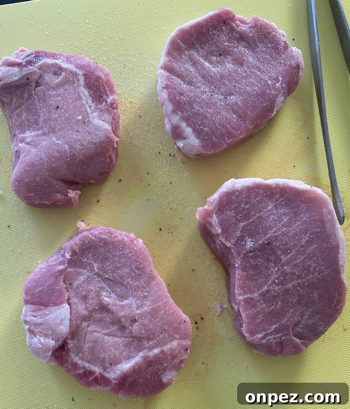 Dutch Oven Pork Chops with Tender Gravy 4 Pork chops seasoned with salt and pepper on cutting board.