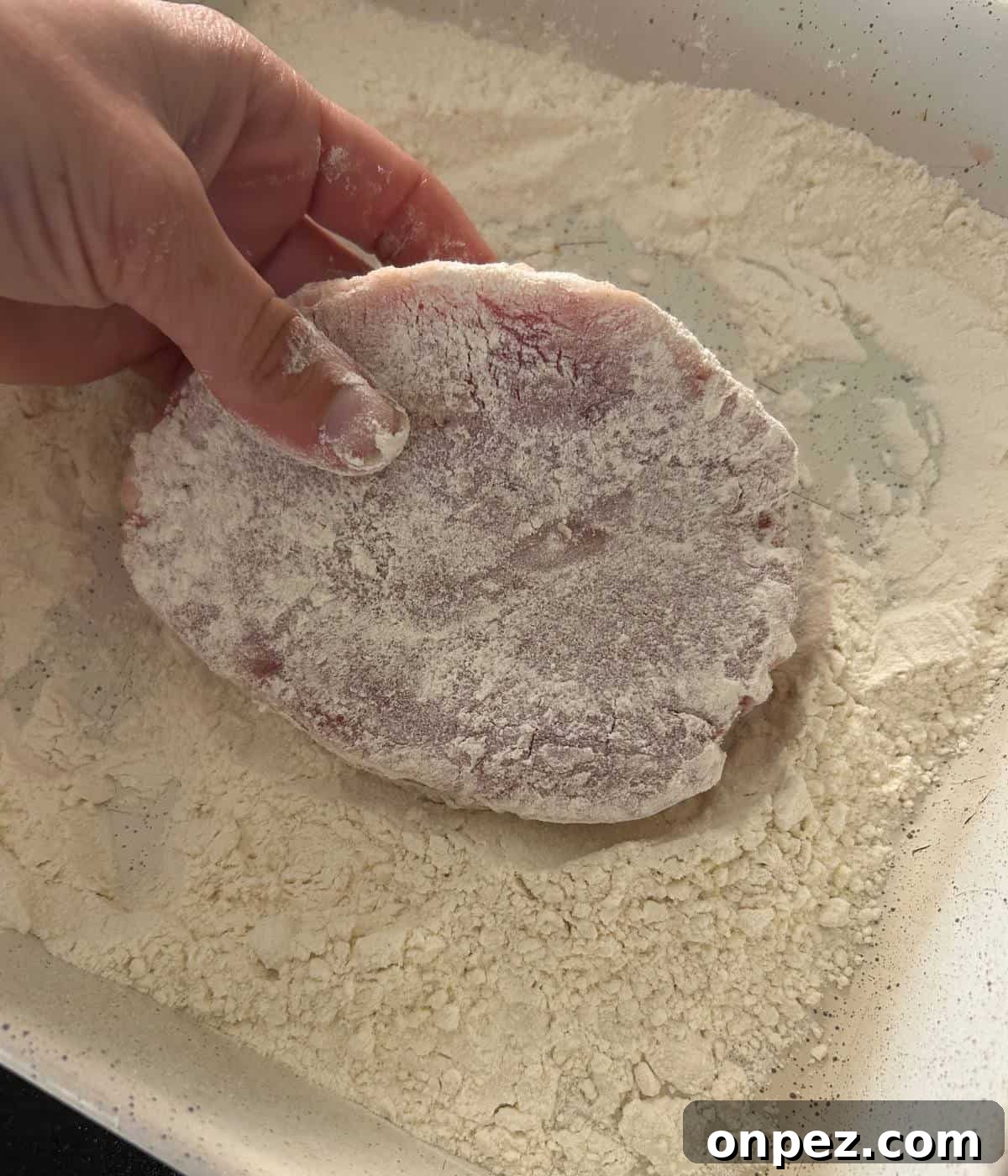 Dutch Oven Pork Chops with Tender Gravy 5 Hand dredging pork chop in flour.
