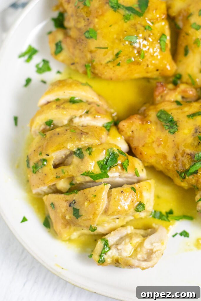 Oven-Baked Maple Mustard Chicken Recipe 2 Maple mustard chicken on a plate with maple mustard sauce topped with freshly chopped parsley. The chicken is cut into slices.
