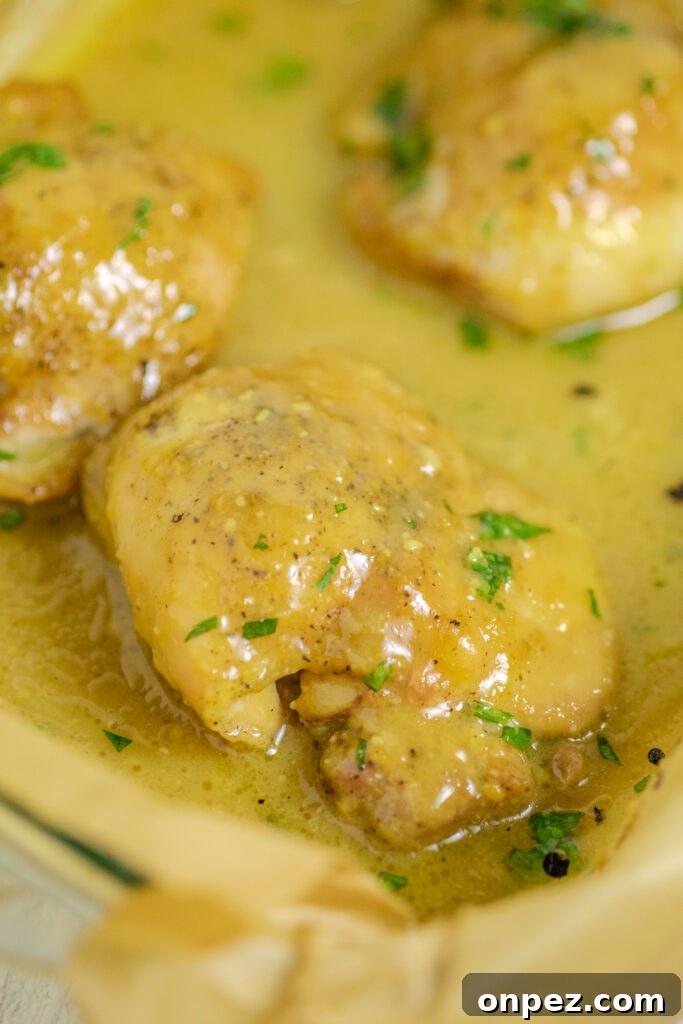 Oven-Baked Maple Mustard Chicken Recipe 3 Maple mustard chicken in a baking dish lined with brown parchment paper and topped with fresh parsley.