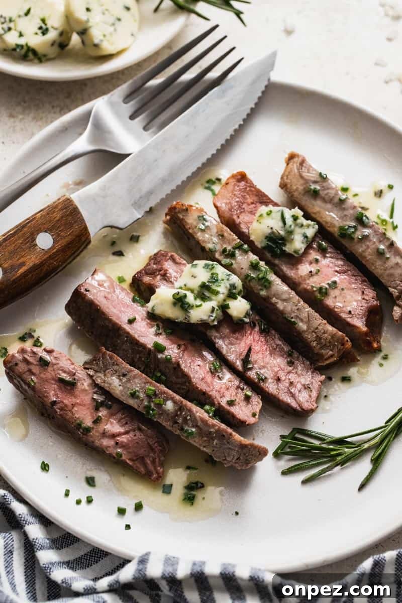 A plate with a fork and knife next to a cooked strip steak that's topped with chives.