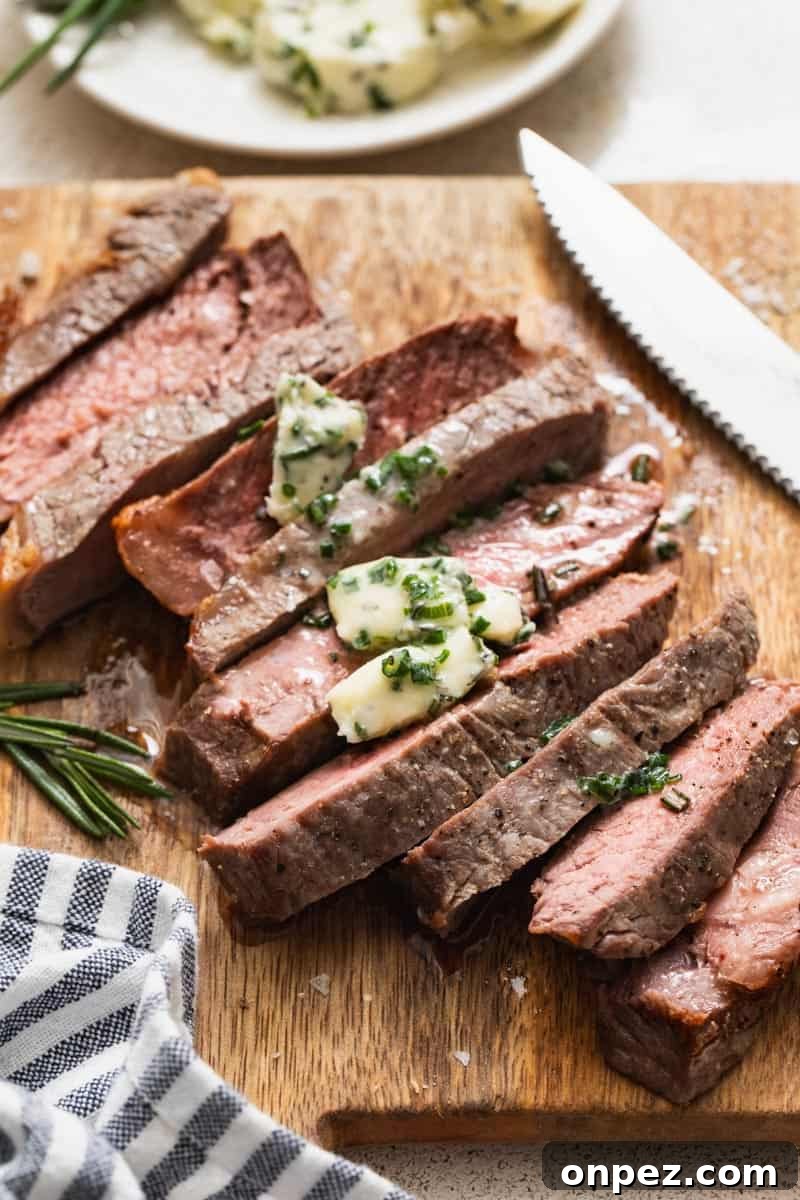 A strip steak with butter on a cutting board with a knife and blue and white napkin.