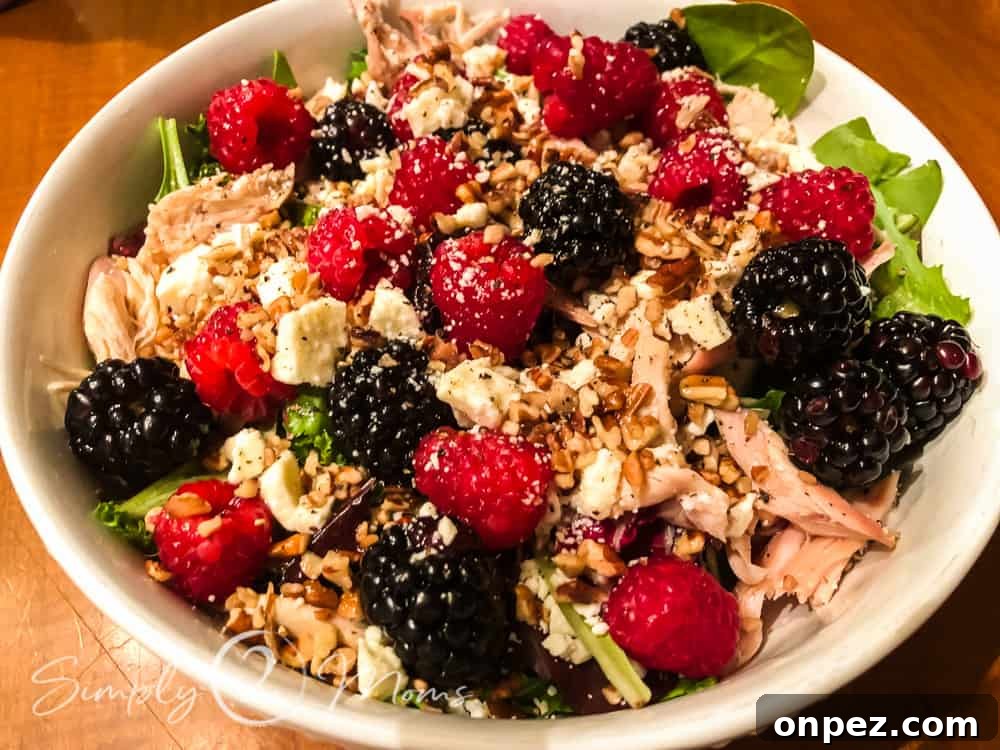 Bowl of mixed greens topped with shredded chicken, fresh raspberries and blackberries, and diced pecans for a delicious healthy summer salad