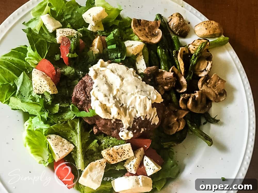 Overhead view of a plate filled with a bed of lettuce with grilled asparagus, grilled mushrooms, fresh mozzarella cheese, and sliced tomatoes topped with a burger spread with boursin cheese