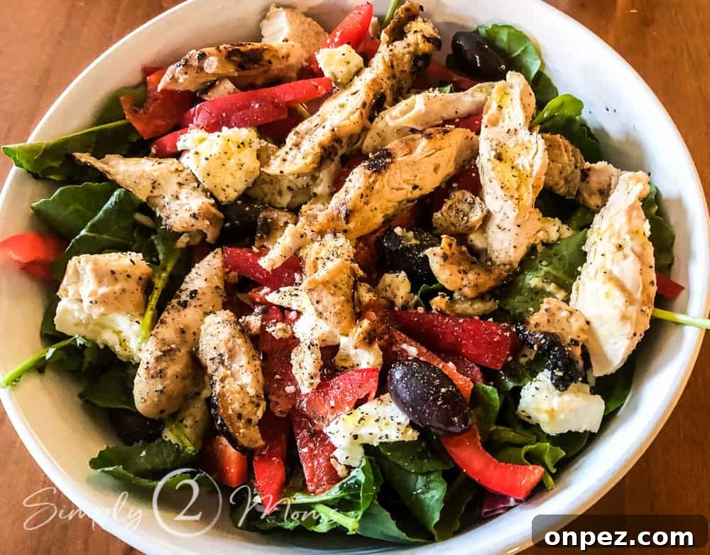 Overhead view of a bowl of baby kale topped with grilled chicken, sliced red bell peppers, kalamata olives, and feta cheese