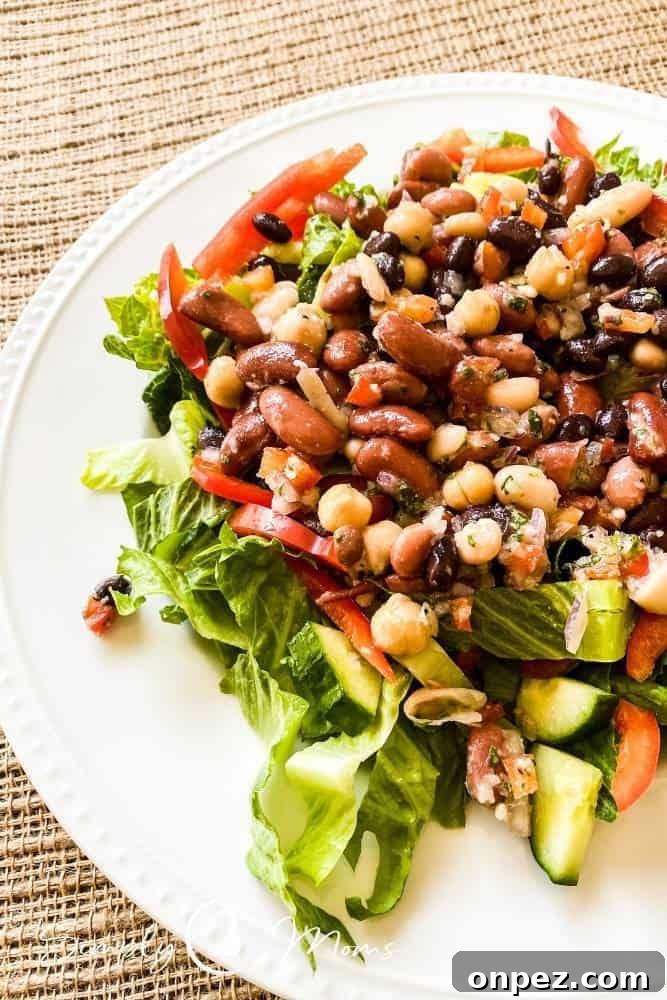 This healthy summer salad consists of a bed of lettuce topped with chopped cucumbers, sliced red bell peppers, chopped tomatoes, and bean salad.