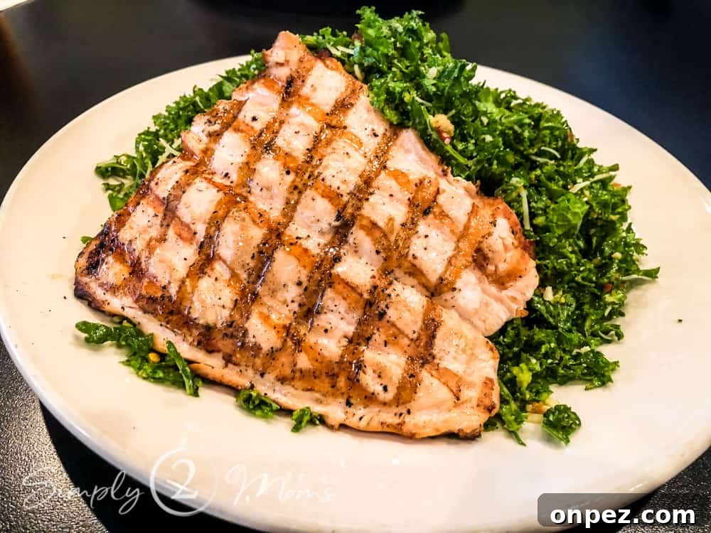 Plate of chopped kale salad topped with grilled salmon and shredded Parmesan cheese.