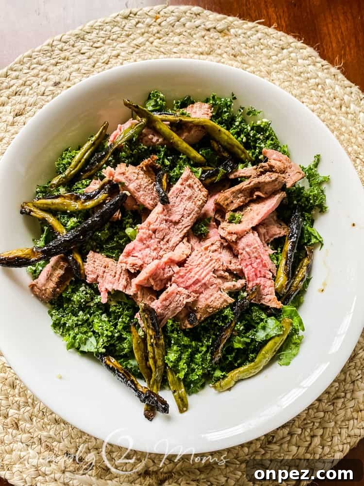 Overhead view of a bowl filled with kale and topped with grilled green beans and sliced steak to make a healthy summer salad