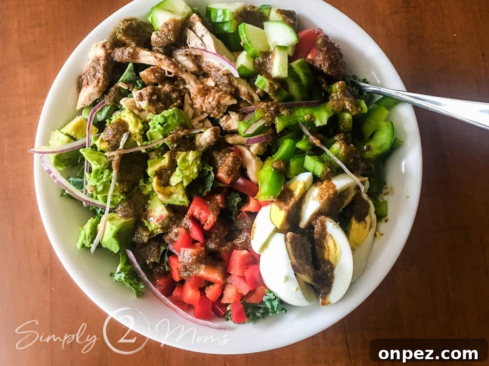 Bowl of chopped Romaine lettuce topped with diced red pepper, diced green pepper, diced cucumbers, thinly sliced red peppers, diced avocado, and a hard boiled egg all drizzled with balsamic vinegar.
