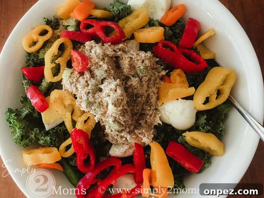 Bowl of fresh kale topped with sliced mini bell pepper rings, hard boiled egg whites, and tuna salad