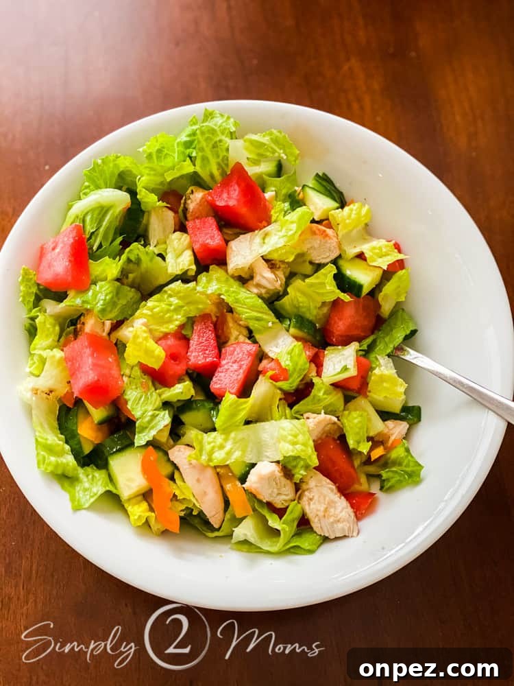 Overhead view of a healthy summer salad made from chopped hearts of Romaine topped with diced watermelon, diced cucumbers, and grilled chicken