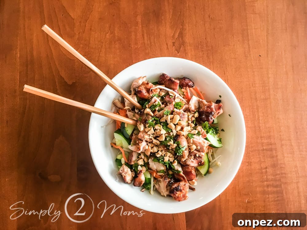 Overhead view of a bowl of konjac noodles topped with diced cucumbers, shredded carrots, bean sprouts, grilled chicken, diced peanuts, and minced cilantro