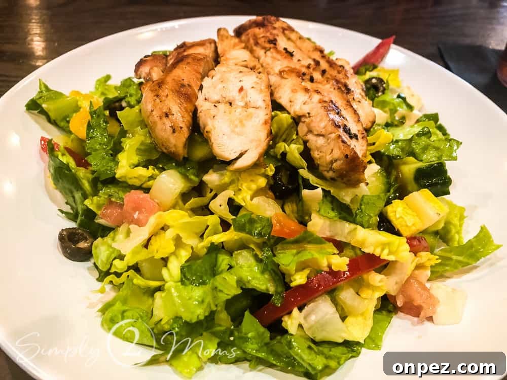 Plate of torn Romaine lettuce topped with diced cucumber, diced tomatoes, sliced red onion, black olives, sliced pepperoncinis, and grilled chicken