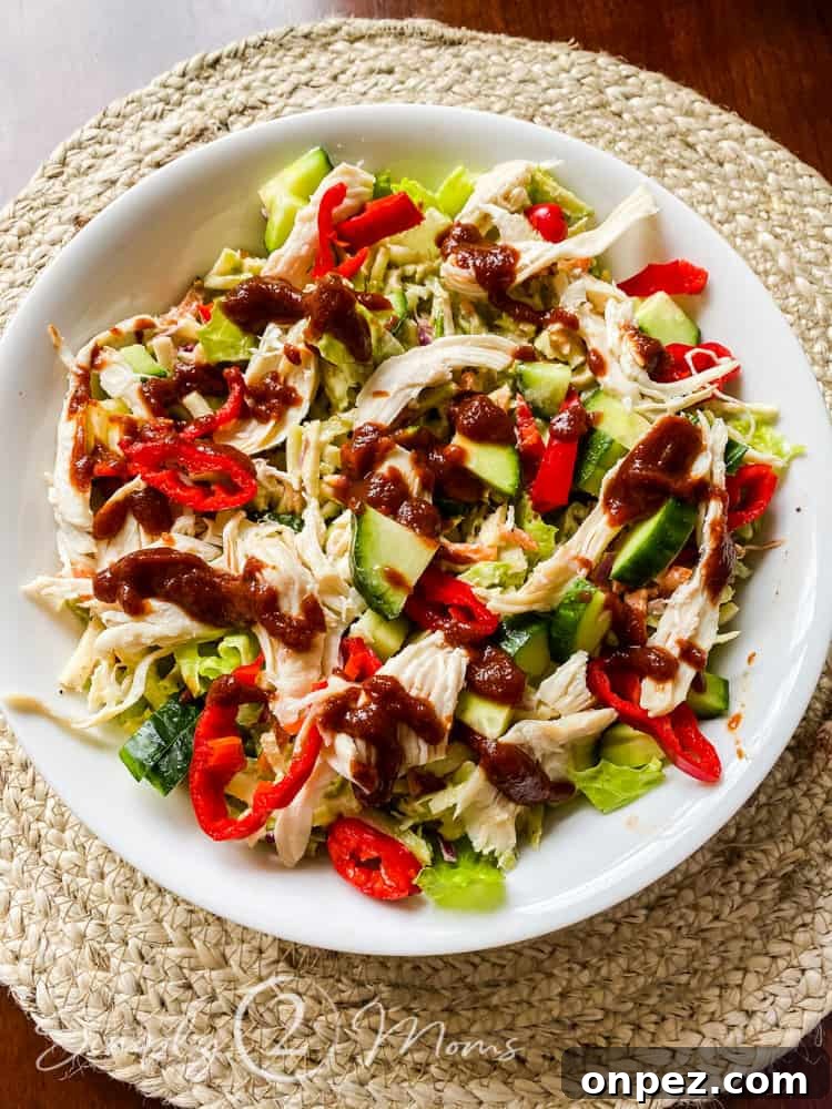 overhead view of a salad made from a bed of lettuce topped with chicken, cucumbers, sliced red peppers, and low carb barbecue sauce