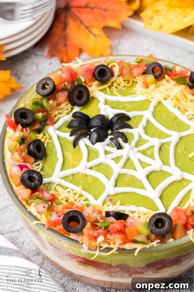 Spider Web 7 Layer Dip is just what your Halloween needs! A spooky little olive spider sits atop a sour cream spider web on layers of meat, beans, cheese, guacamole, and more!