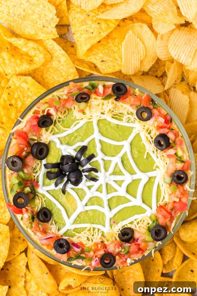 Spider Web 7 Layer Dip is just what your Halloween needs! A spooky little olive spider sits atop a sour cream spider web on layers of meat, beans, cheese, guacamole, and more!