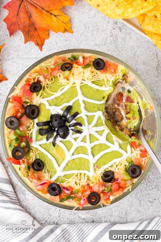 Spider Web 7 Layer Dip is just what your Halloween needs! A spooky little olive spider sits atop a sour cream spider web on layers of meat, beans, cheese, guacamole, and more!