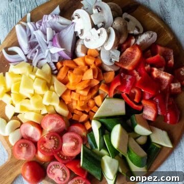Assortment of colorful chopped vegetables on a round wooden board.
