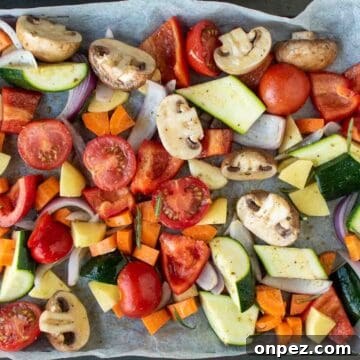 Assorted chopped vegetables in a single layer on a baking sheet viewed from above.