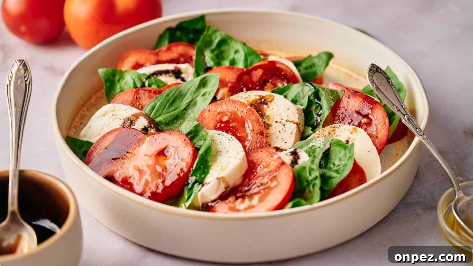 Caprese salad in a serving bowl, with tomatoes, oil and balsamic glaze nearby.