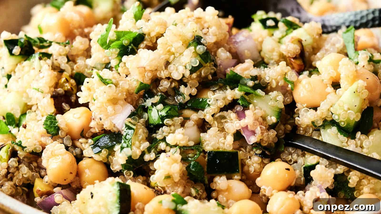 Close-up of a quinoa salad with chickpeas, chopped cucumber, parsley, red onion, and a light dressing, with a spoon partially visible.
