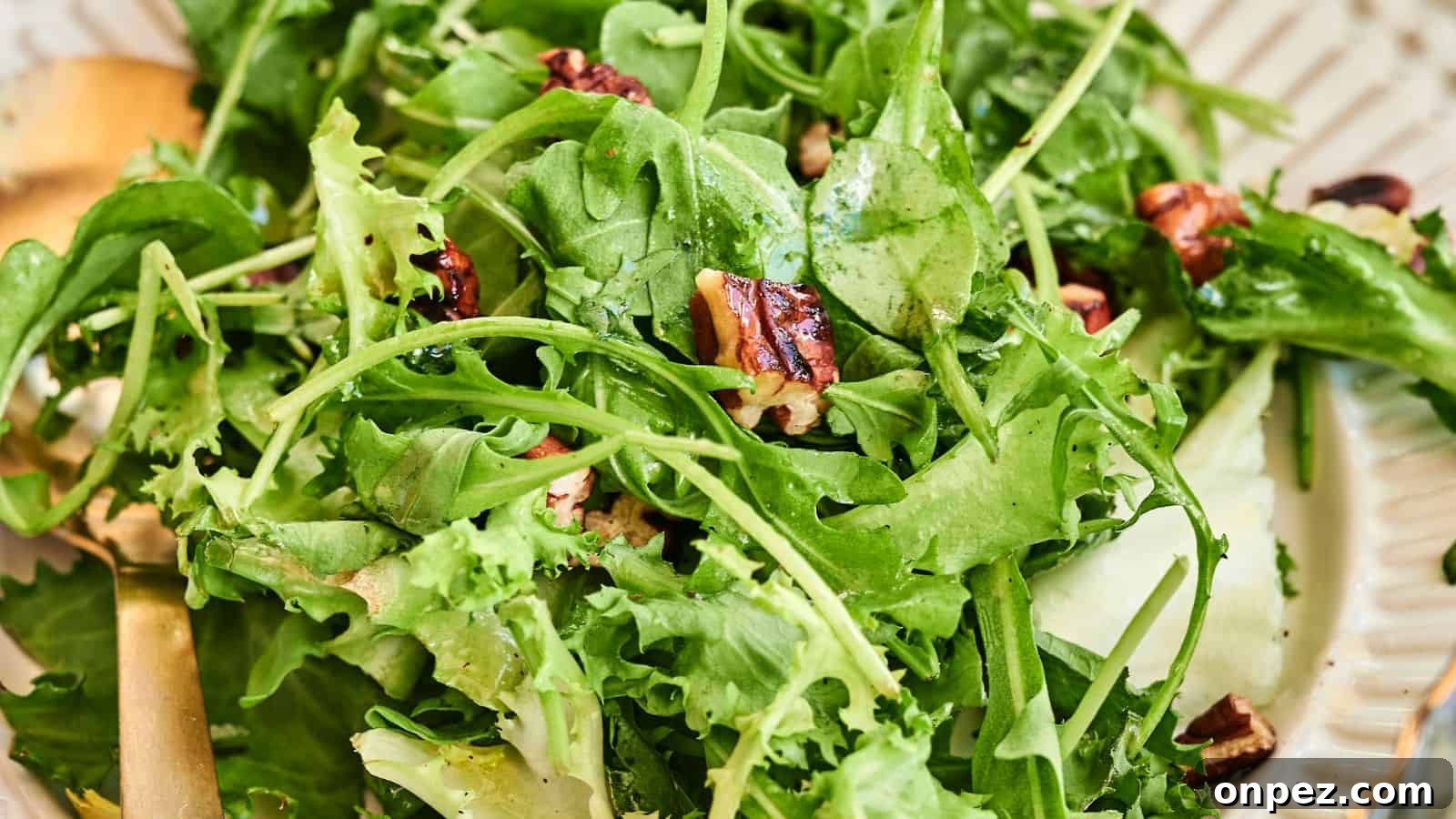 A close-up of a fresh green salad with mixed leafy greens, cucumber slices, and pecans on a plate with a gold fork.