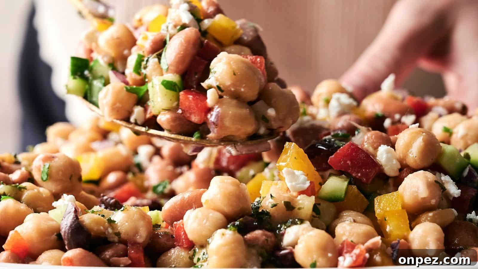 A spoonful of chickpea salad with chopped cucumbers, tomatoes, peppers, parsley, and feta cheese being served from a bowl.