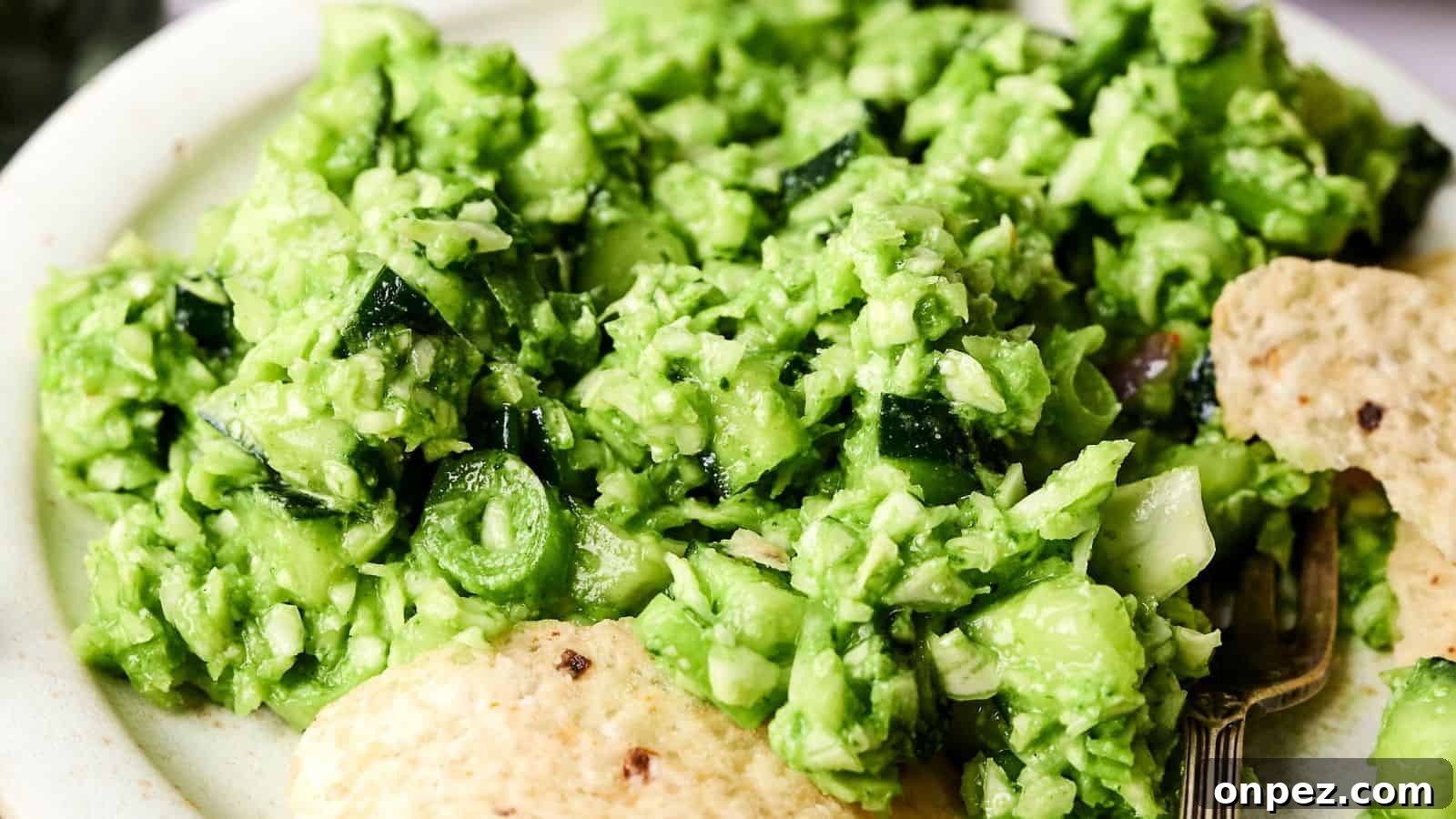 A close-up of a plate with bright green guacamole, chopped vegetables, and tortilla chips on the side.