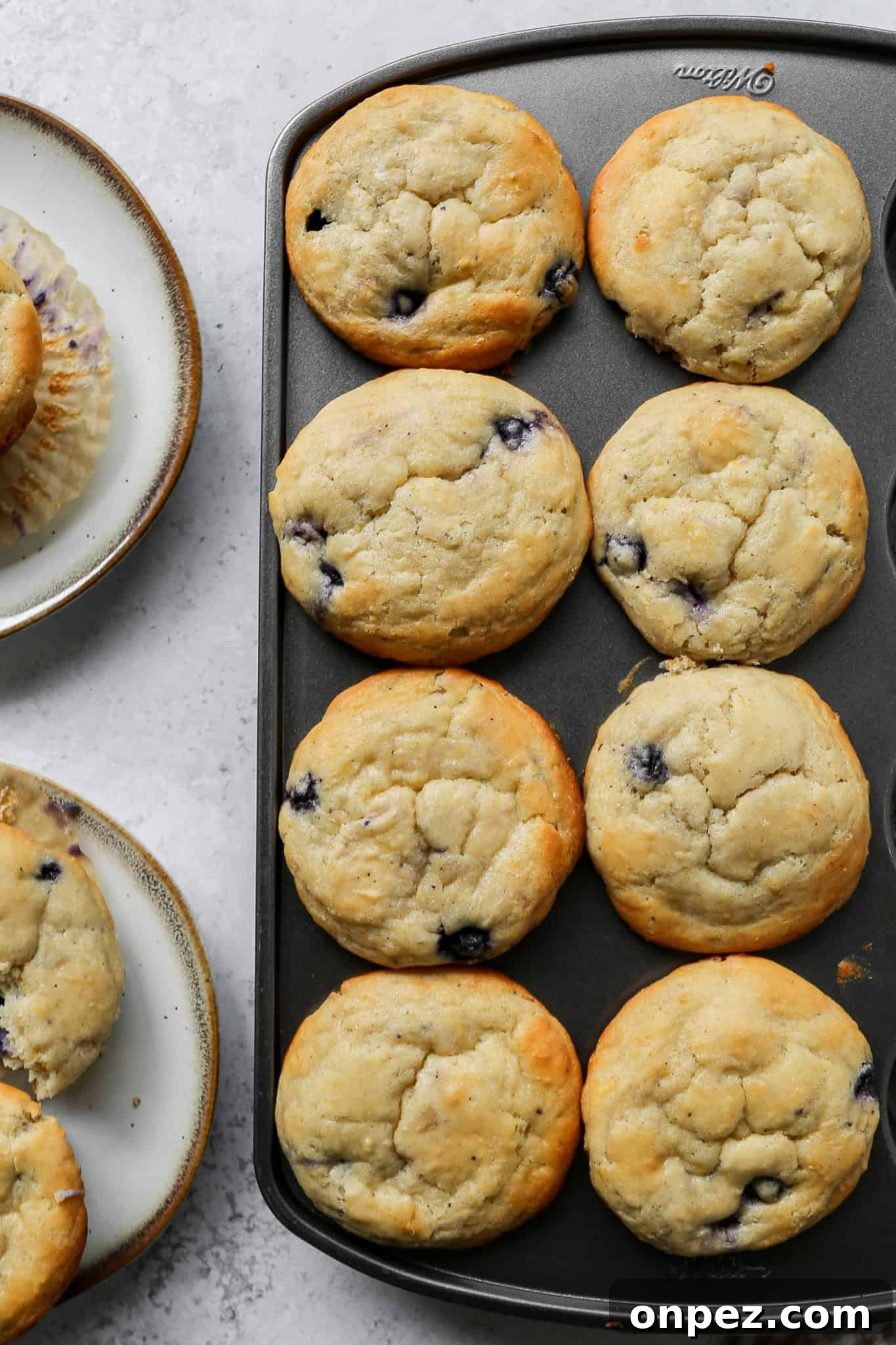 Gluten-Free Lemon Blueberry Muffins Recipe 3 a wilton muffin pan with eight gluten free lemon blueberry muffins in it next to two small plates of muffins