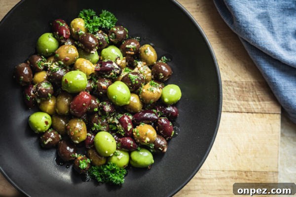 Garlic and Herb Marinated Olives Recipe 4 Green and black marinated olives with herbs, spices, garlic, oil and vinegar with parsley in a black bowl