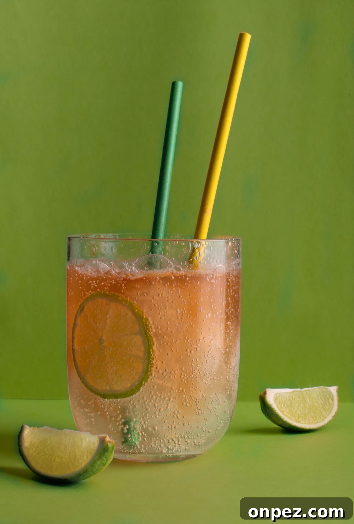 Classic Lemon Lime and Bitters Cocktail Recipe 2 A glass of lemon, lime and bitters with two straws, on a green background.