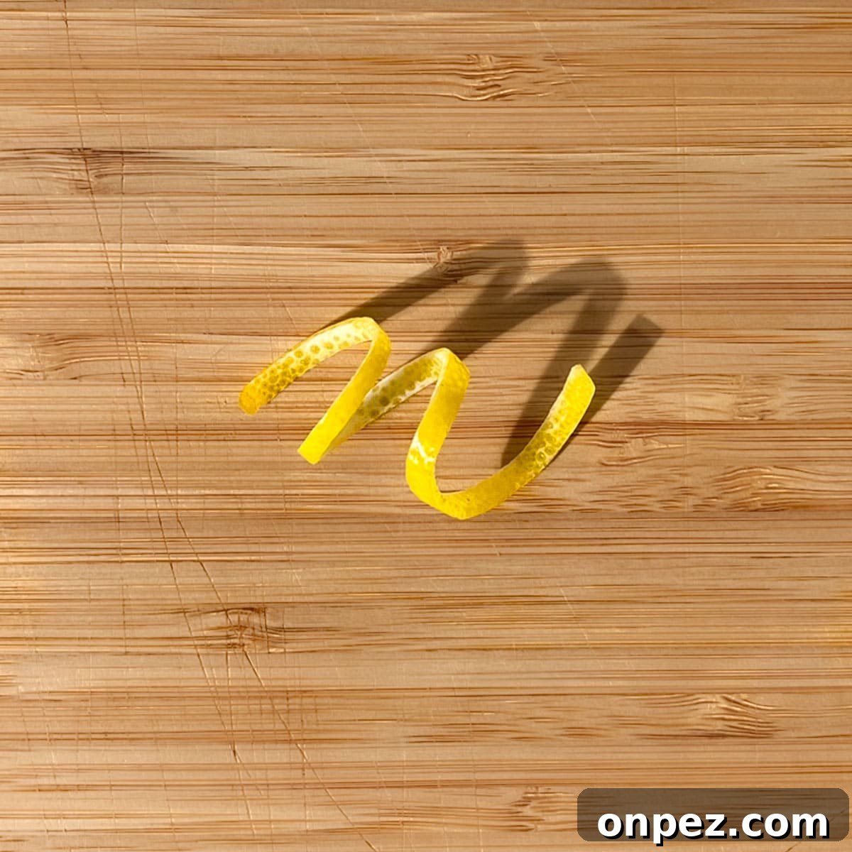 Classic Lemon Lime and Bitters Cocktail Recipe 11 A lemon peel twisty on a wooden chopping board.