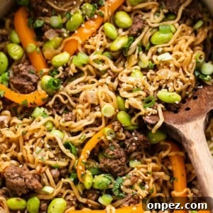 A pan full of noodles and vegetables with a wooden spoon.