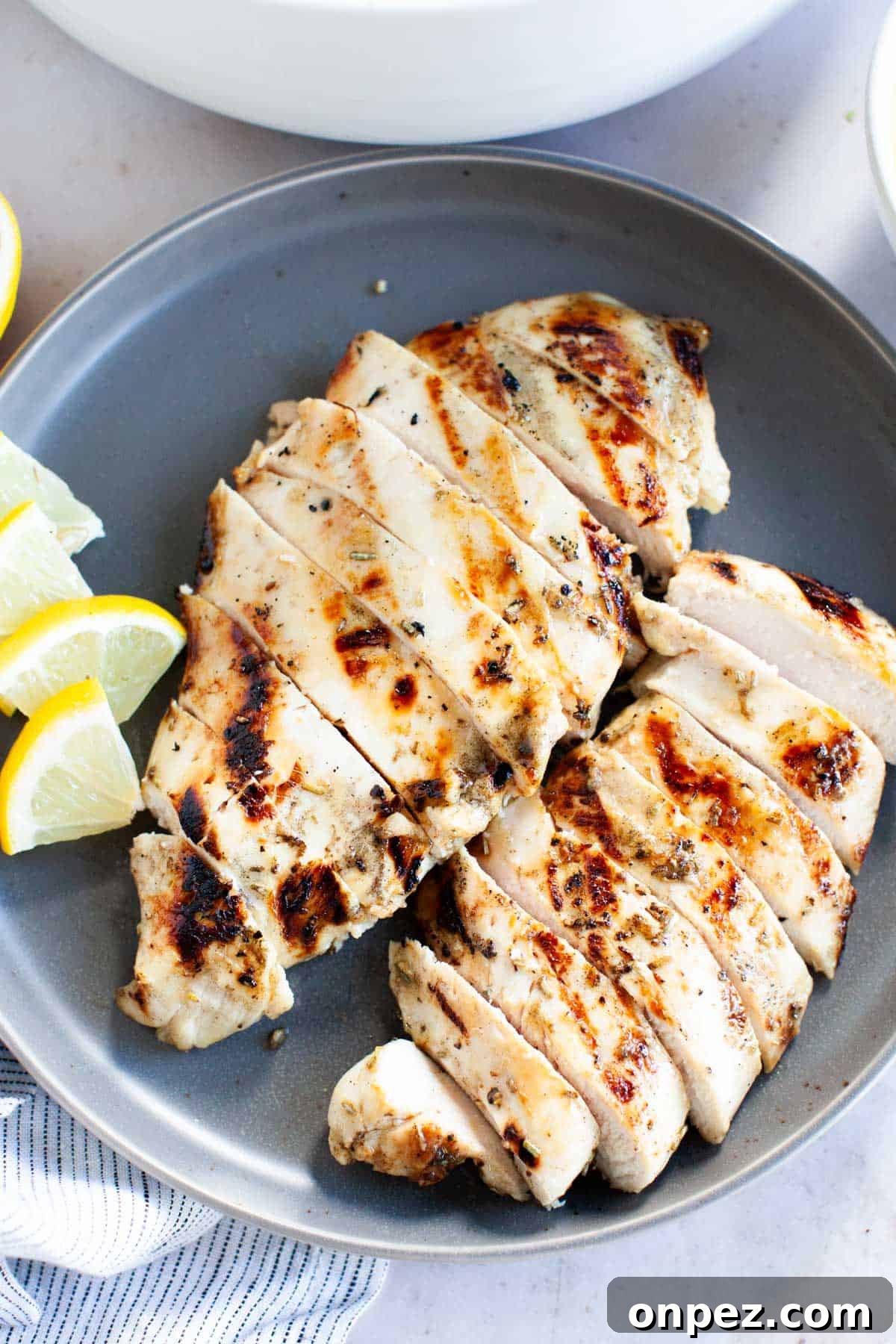 Thinly, sliced grilled chicken breasts with lemon wedges on a small, gray plate.
