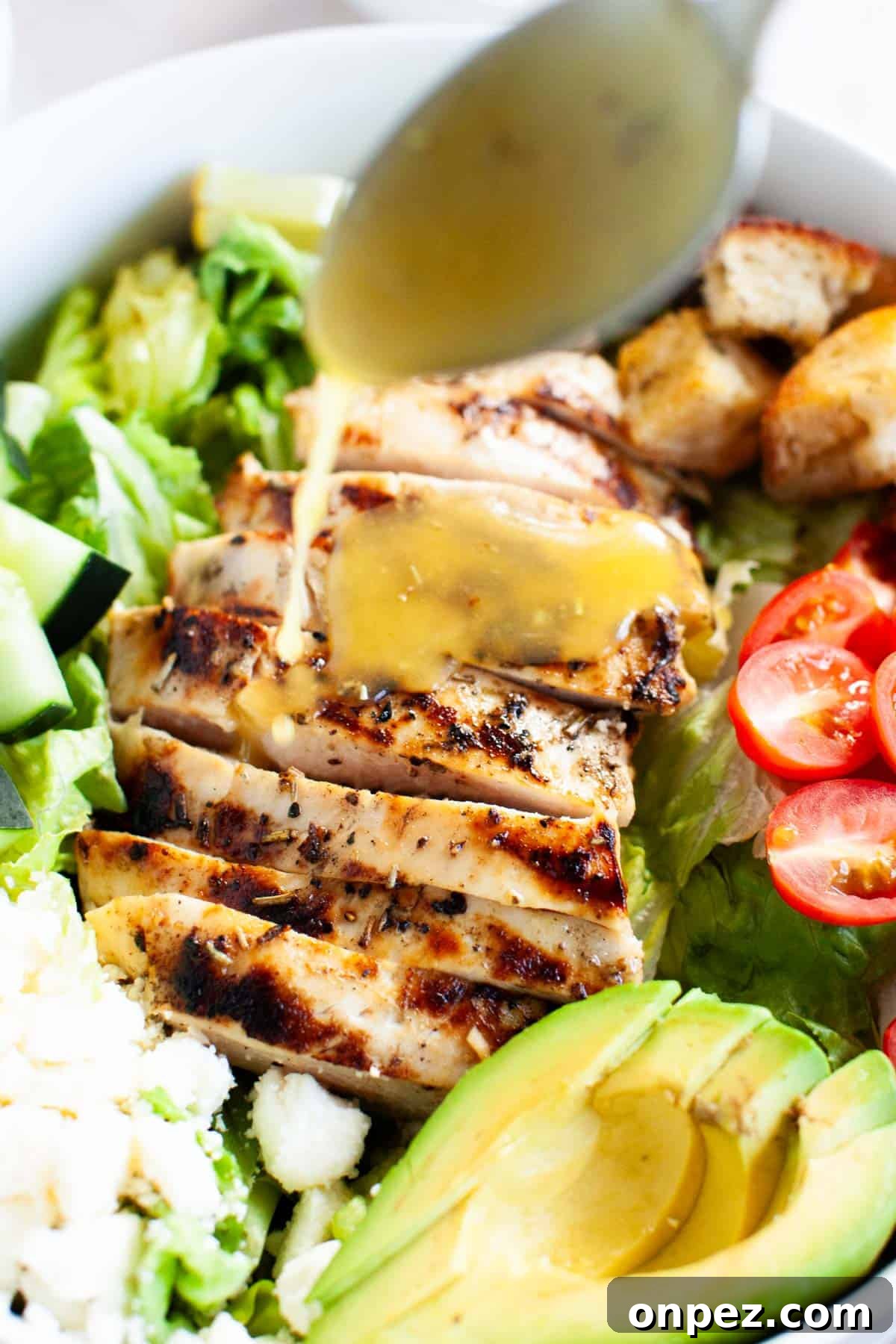 A honey vinaigrette dressing being drizzled onto the grilled chicken salad.