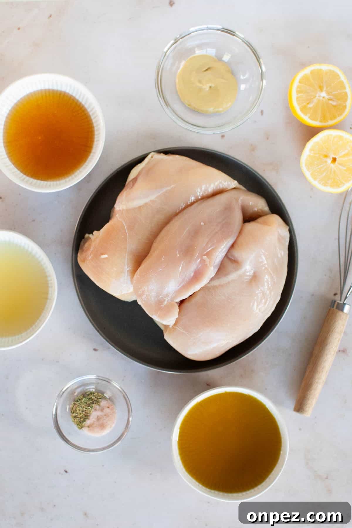 Honey vinaigrette ingredients in small, individual bowls accenting a plate of raw chicken breasts.