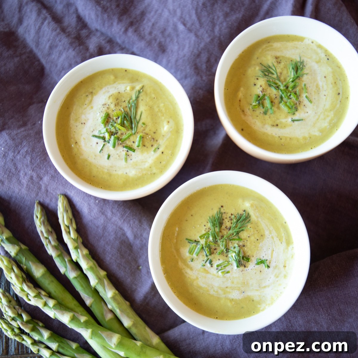 Keto Cream of Asparagus Soup: Low-Carb, Creamy Recipe 2 3 bowls of cream of asparagus soup, garnished with chives and fresh dill. A few asparagus are off to the side.