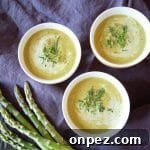 3 bowls of cream of asparagus soup, garnished with chives and fresh dill. A few asparagus are off to the side.