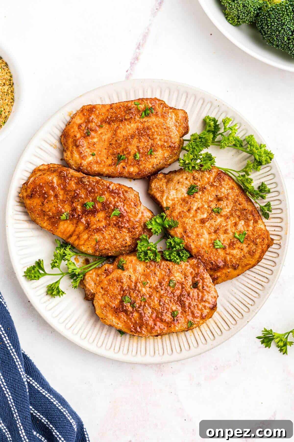 Air fryer frozen pork chops on a white plate with parsley sprinkled on top.