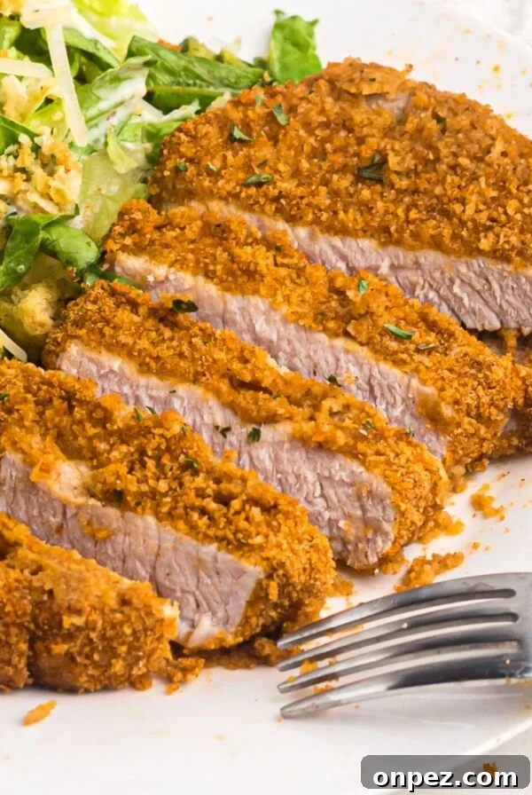 Golden crispy pork chop sliced on a white plate with salad and a fork
