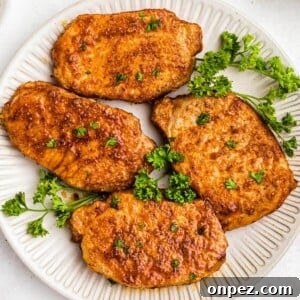 Frozen pork chops in the air fryer on a white plate with parsley garnish.