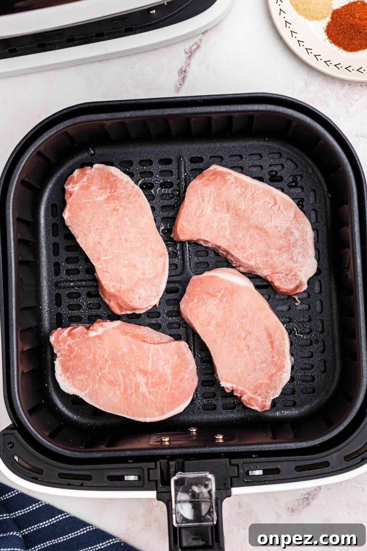 Frozen pork chops in air fryer basket before being air fried.