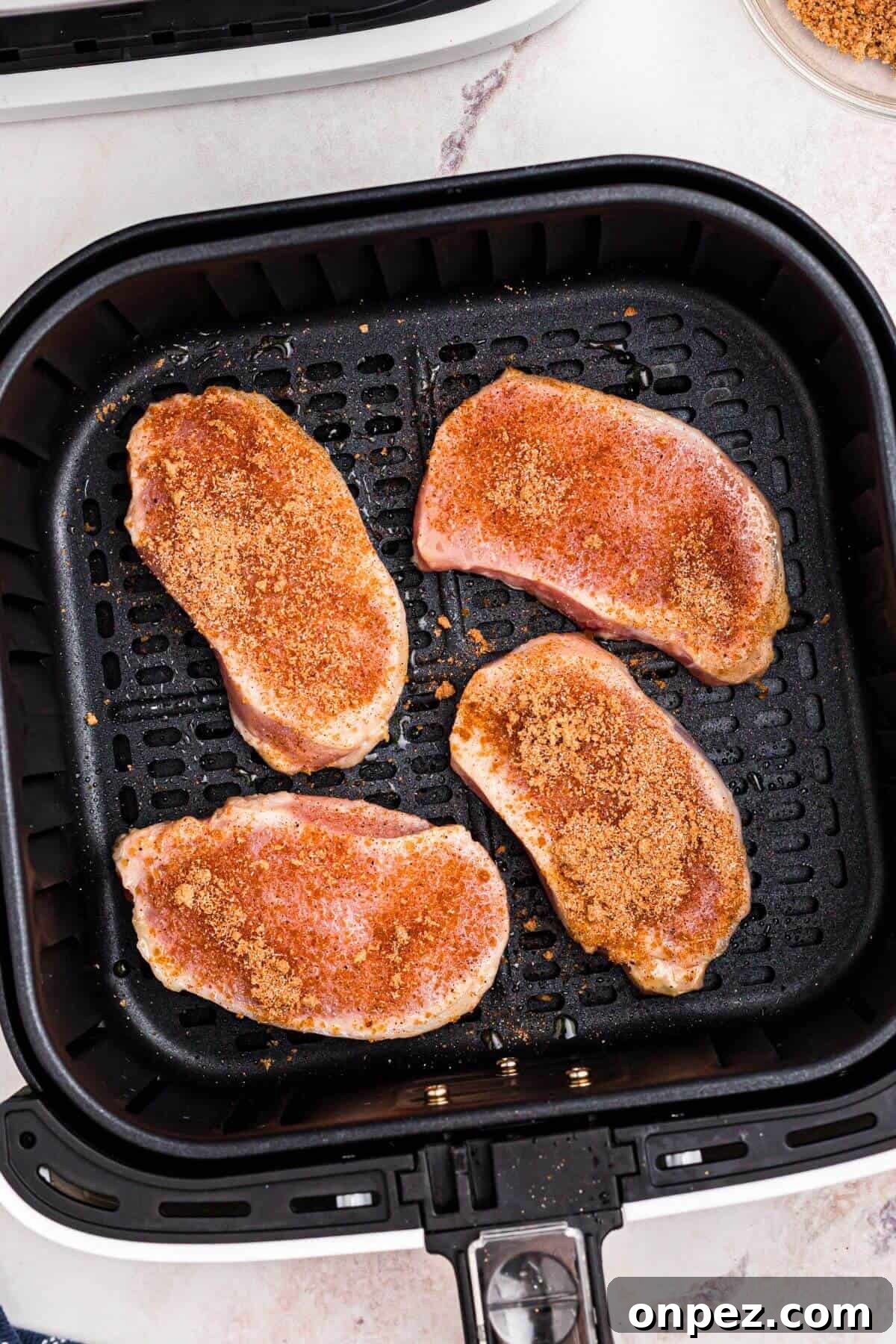 Uncooked pork chops in the air fryer with seasoning added on top.
