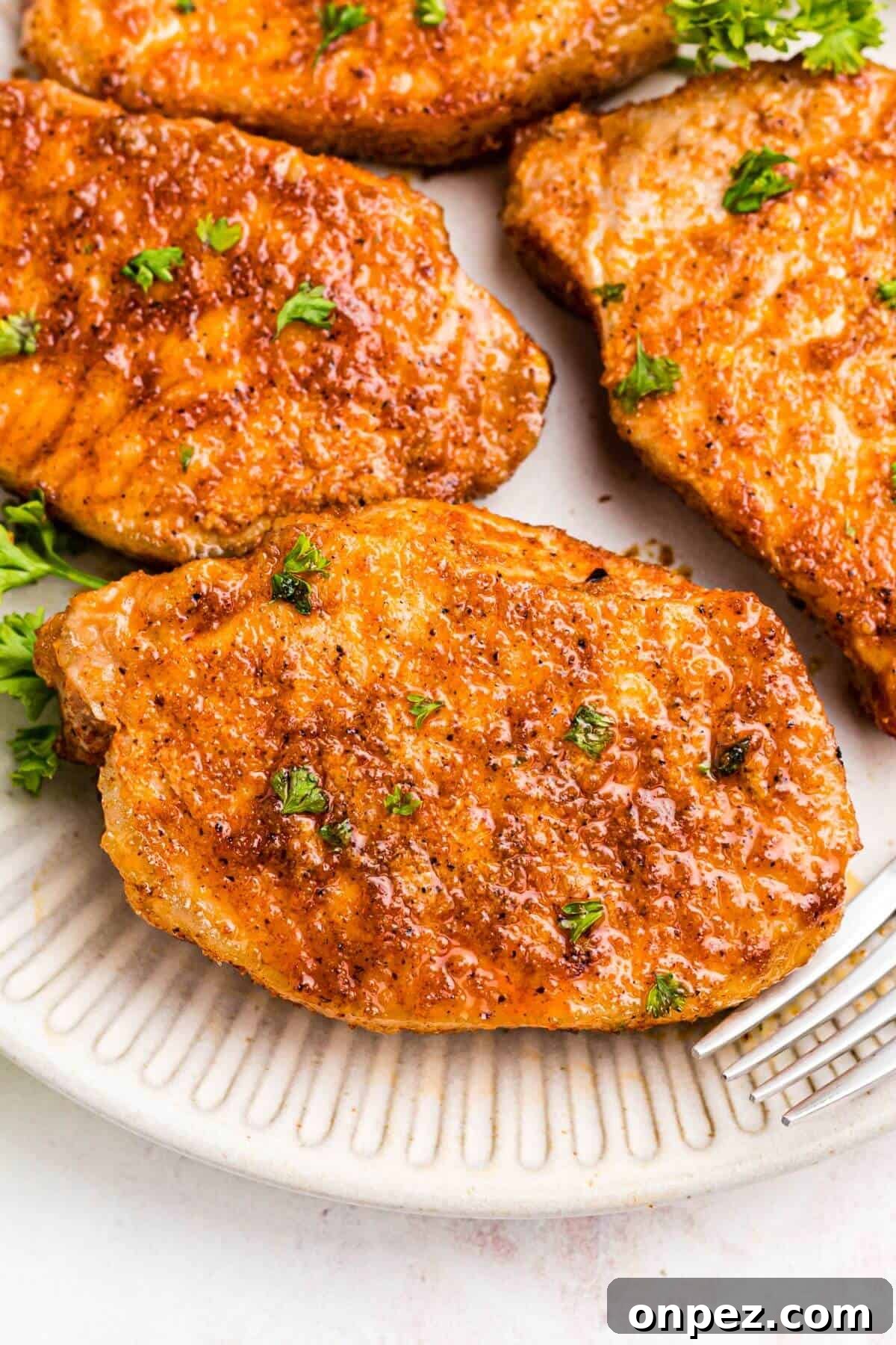 Air fryer frozen pork chops on a white plate with a fork and parsley garnish.