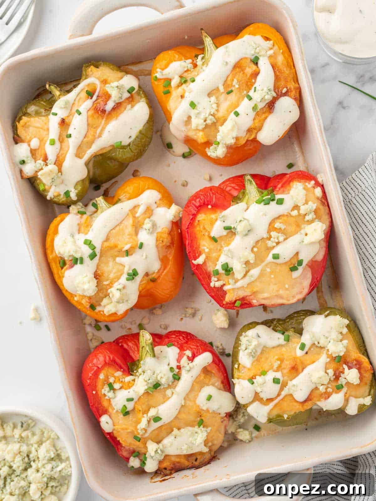 Buffalo Chicken Stuffed Bell Peppers 2 Healthy chicken stuffed peppers topped with ranch and crumbled blue cheese in a baking dish.
