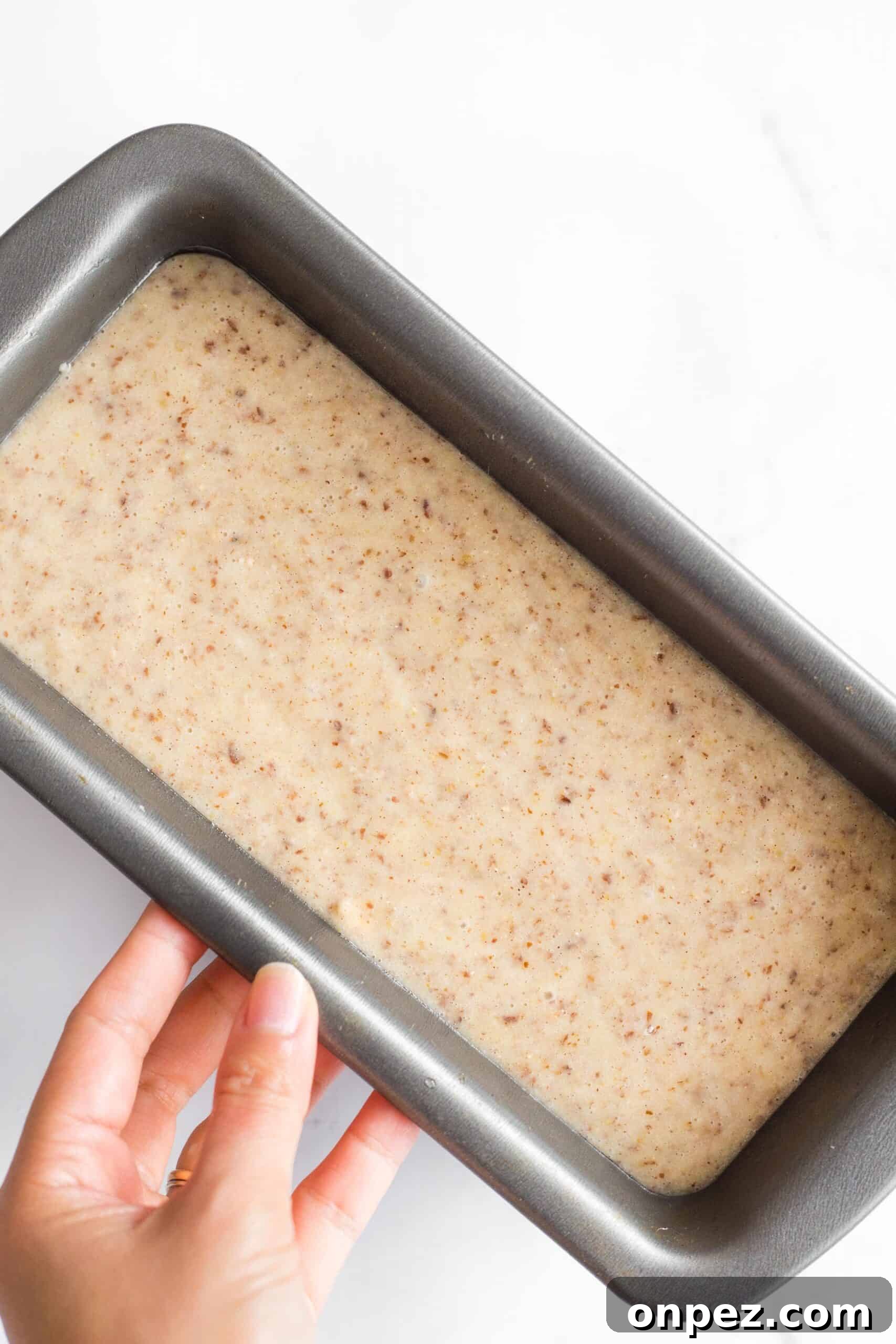 Easy Flax Bread Recipe (Gluten-Free, Dairy-Free) Hand holding a metal loaf pan with flax bread batter.