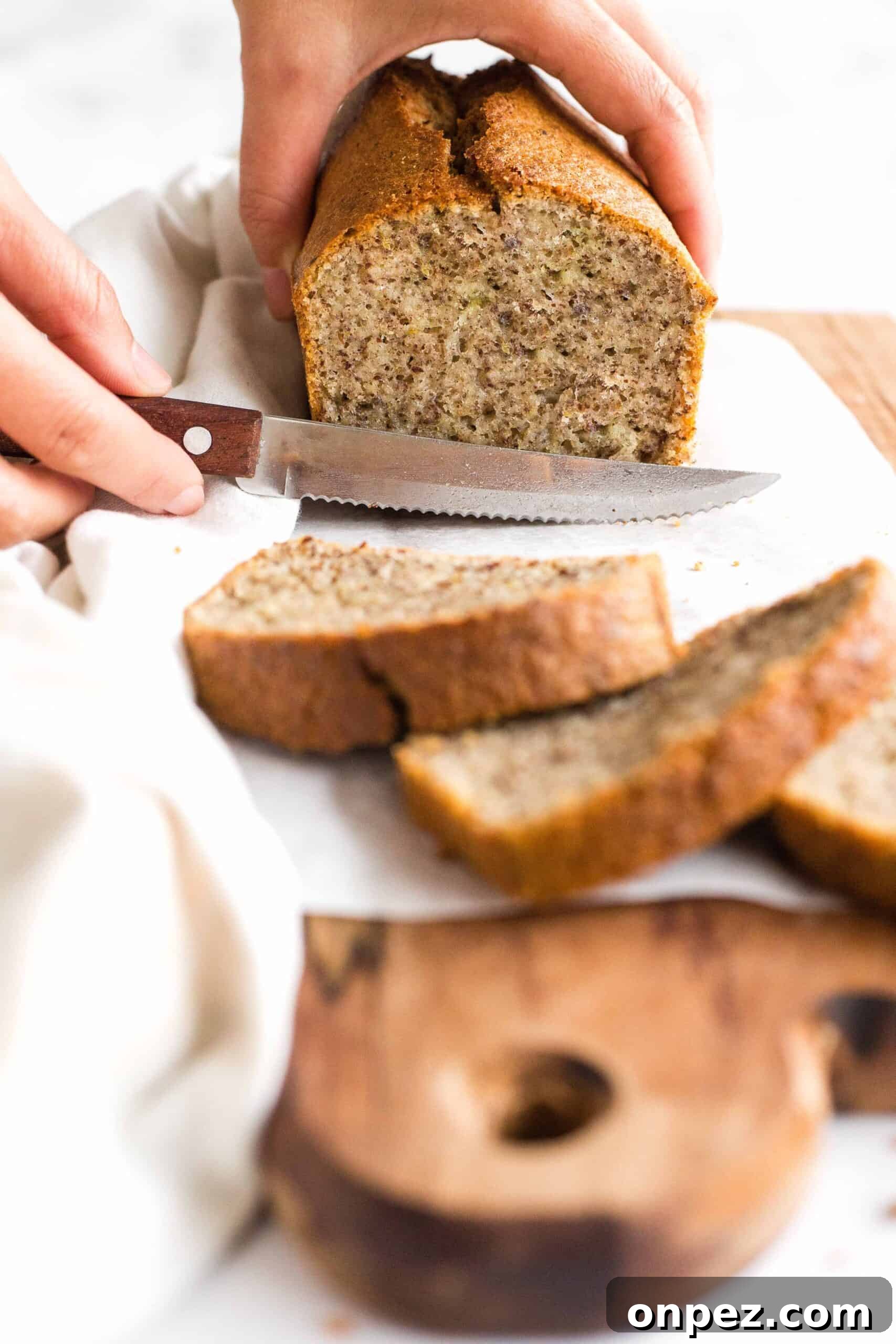Easy Flaxseed Bread (Gluten-Free, Dairy-Free) Slicing into a loaf of flaxseed bread on a wooden board.